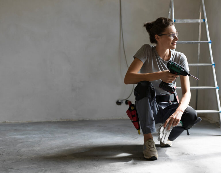 Professional repairwoman with tool belt doing a home renovation, she is posing and holding a drill