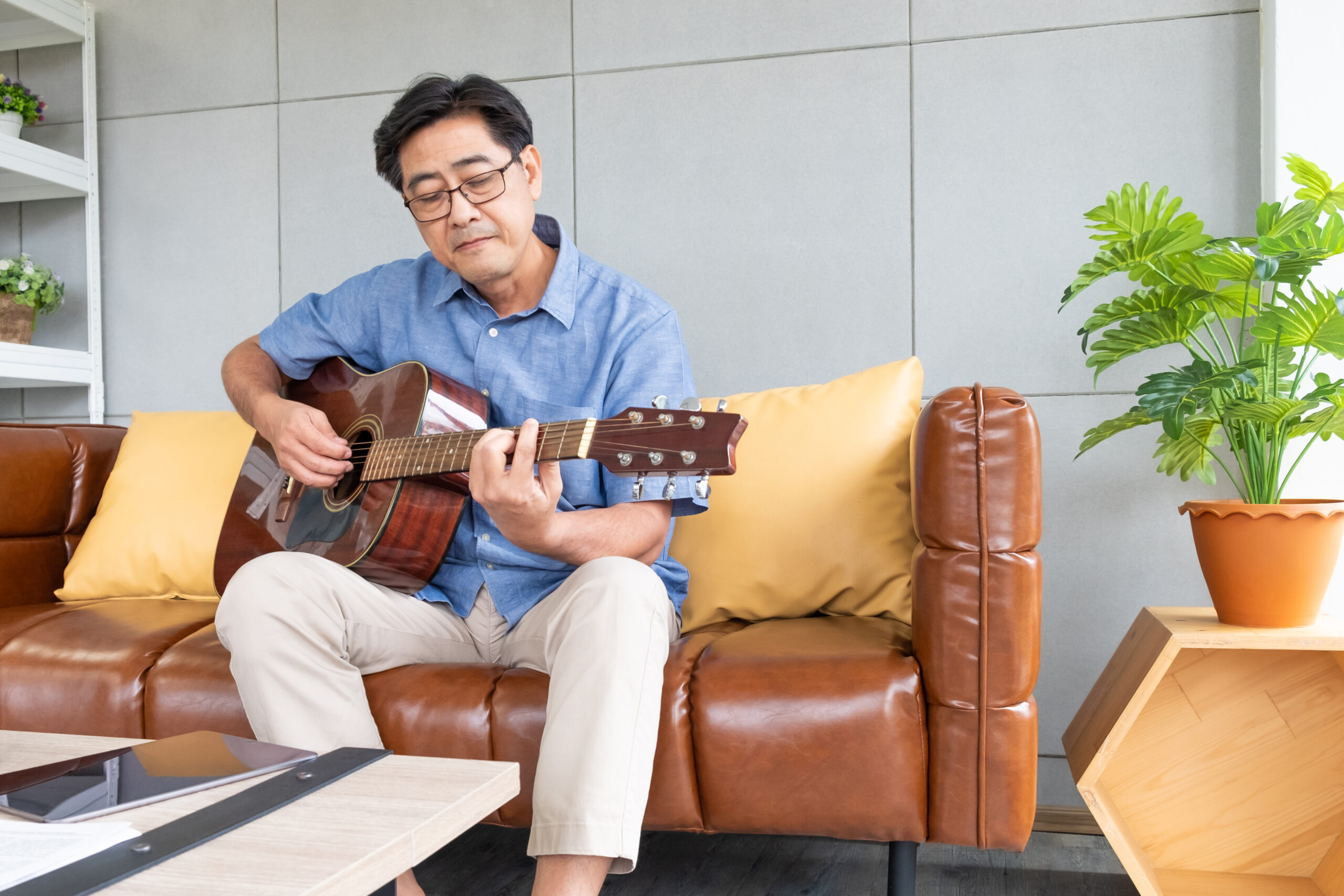 Asian man with guitar on brown couch