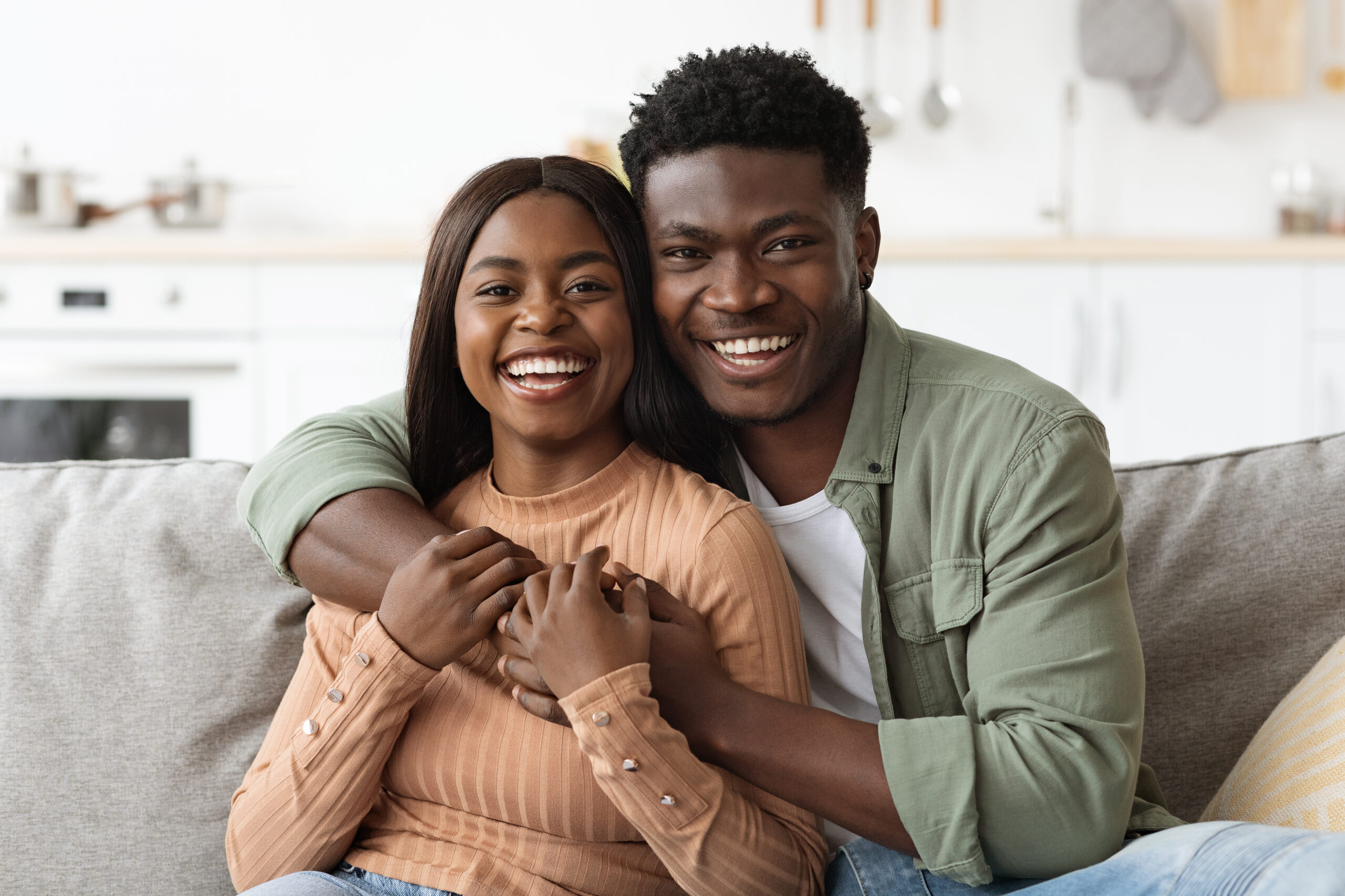 Closeup portrait of happy black couple embracing and smiling at camera, loving man and woman sitting on couch in living room, enjoying weekend together, home interior, copy space